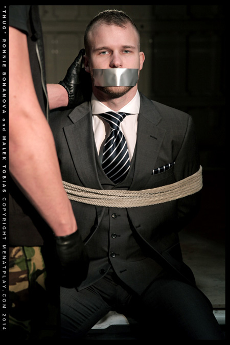 Blue-eyed businessman in a suit tied up with rope and his mouth closed shut with duct tape.
