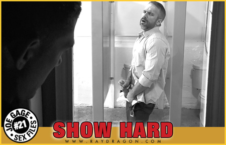 Bearded man masturbating in a public bathroom in front of a one-way mirror.